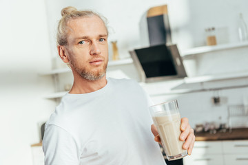 athletic man holding glass with protein shake and looking at camera