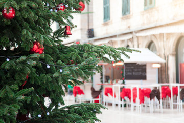 Christmas tree with red ornaments on market outside. Street cafe in old town. Cozy festive atmosphere in Dubrovnik, Croatia.