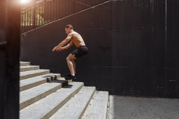 Fototapeta premium Cute caucasian shirtless jumper in motion, flying over the stairs, doing crossfit training outdoors. Healthy lifestyle, sport and people.