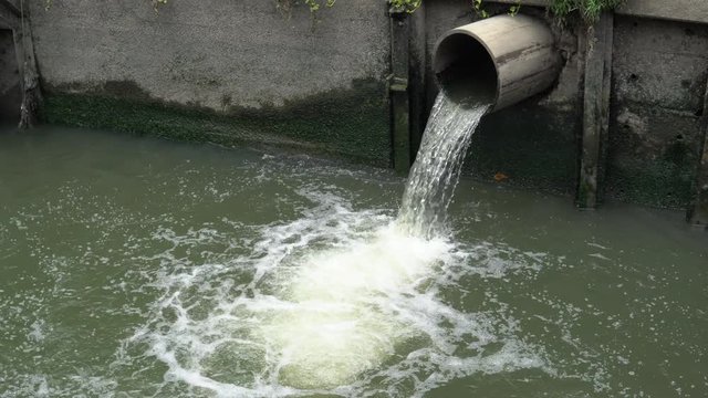 Water flows down from sewer into polluted pond in city