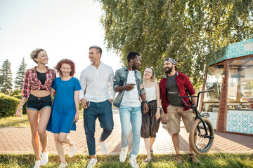 Fototapeta premium Happy multiethnic friends being glad to be together at urban park outdoors, spend leisure time in entertainment outdoor center.