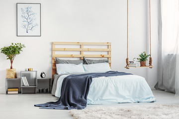 Bright bedroom interior with king size bed with light blue bedding and warm blanket, copy space on white wall