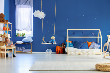 Blue wall with golden stars in stylish scandinavian kid room with wooden house shape bed with pillows