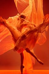 Young graceful female ballet dancer or classic ballerina dancing at red studio. Caucasian model on pointe shoes