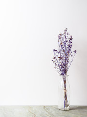 Bouquet of dried and wilted purple Gypsophila flowers in glass bottle on matt marble floor and white background with copy space
