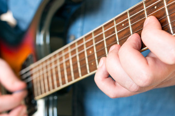 Fototapeta premium Hands of a man in a denim shirt playing vintage sunburst guitar