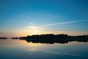 A beautiful and calming sunset accented by a long narrow cloud, a few days after midsummer, reflected on the water of a cove on the Island of Nicklösa in the Åland Islands, Finland.