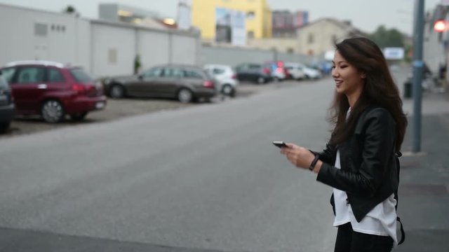 Young beautiful asian woman standing outdoor in the city, using smart phone and hitchhiking – technology, social network, communication concept	