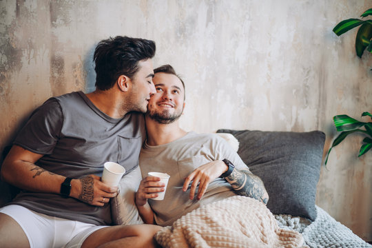 European happy gay couple drinking tea while having fun in bed , caressing and watching movies. Homosexual relationships and alternative love lifestyle concept - Powered by Adobe