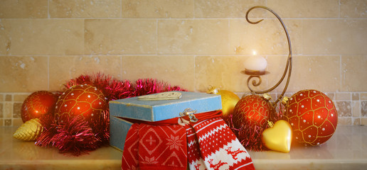 Christmas and New Year decorations: christmas red and golden balls, candle and gift box on the mantelpiece.