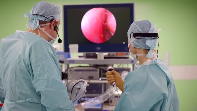 male and female neurosurgeons are performing endoscopic operation, watching inside view on a display