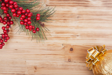 Holiday decoration - pine and berry bush with Italian chocolate ball wrapped in metallic gold foil and topped with golden ribbons and bows on wooden background