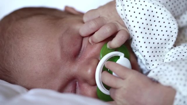 Little 2 weeks old newborn boy lies on the bed. Newborn baby sleeps with pacifier in his mouth. Asleep newborn baby boy