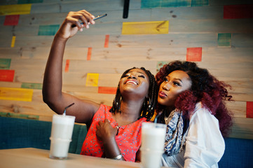 Attractive african american two girls friends sitting at cafe with latte and making selfie on mobile phone.