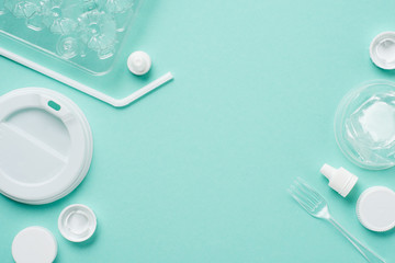 Top view of plastic bottle caps, drinking straw, fork, eggs tray and lid for drink on blue background