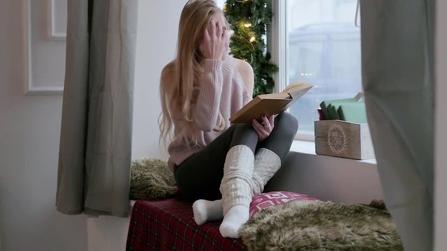 young blond woman in leggings sitting on the window. to read a book. christmas interior