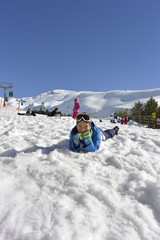 Un chico lindo en un traje de esquí juega bolas de nieve y esculpe un muñeco de nieve.