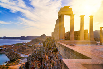 Greece. Rhodes Island. Sun's rays cut through the columns Acropolis of Lindos. View from the height of the ancient temple of Athena Lindia IV century BC to St. Paul's Bay in the form of the heart