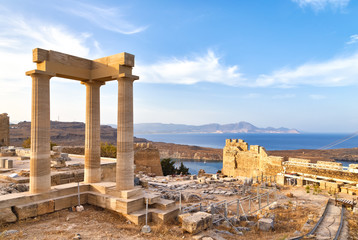 view of the ancient porticos of the temple of the goddess linda in Lindos, Rhodes Greece, overlooking the mountains and a surprisingly beautiful bay
