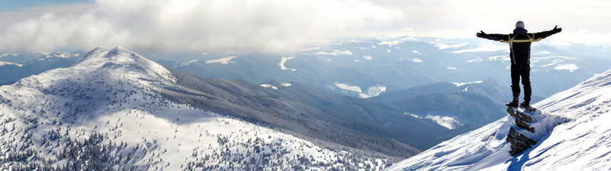 Silhouette of alone tourist standing on snowy mountain top in winner pose with raised hands...