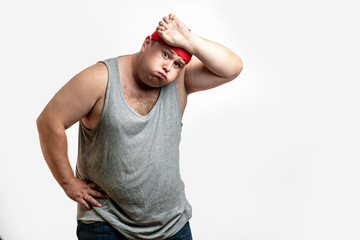 Obese unsporting non- athletic man during his training session, resting, exhausted, taking a overwork, wipes sweat with hand from his forehead against white background. I - obrazy, fototapety, plakaty