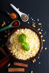 Food concept cooked Couscous in brown ceramic bolw and spices on black slate  board background