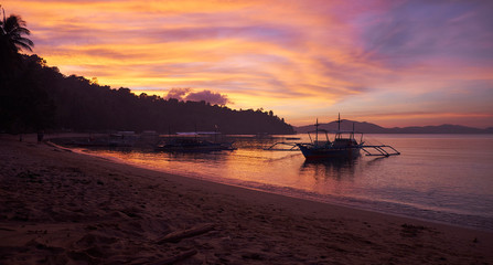 Fototapeta na wymiar Outstanding light at sunset on the beach of the tropical remote fishing village of Port Barton in Philippines, with bobbing boats on water. Long exposure to create soft effect 