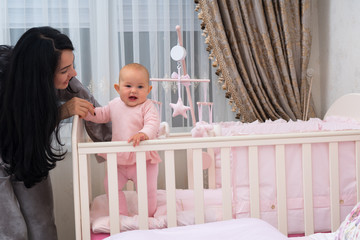 Young mother helping her little daughter stand