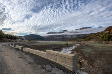 Old road over a ruined bridge that is generally flooded by the waters of the reservoir of Riaño in Leon, Spain. In the background you see the mountains between the morning mists. 