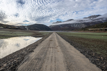 Old road in ruins that is generally flooded by the waters of the reservoir of Riaño in Leon, Spain. In the background you see the mountains between the morning mists.  - obrazy, fototapety, plakaty
