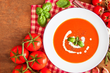 Tomato Soup composition with fresh tomatoes, basil leaf and garlic on a wood table, view from above. Vegetarian Autumn Food