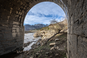 Fototapeta na wymiar View through the arch of a bridge in ruins of the valley flooded by the riaño reservoir, in Vegacerneja, Leon (Spain). In the background you can see the mountains of the area.