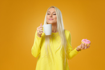Woman holding colorful donut with sprinkles on a yellow background. Cup of coffee. Concept of food and Tasty