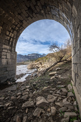 View through the arch of a bridge in ruins of the valley flooded by the riaño reservoir, in Vegacerneja, Leon (Spain). In the background you can see the mountains of the area.
