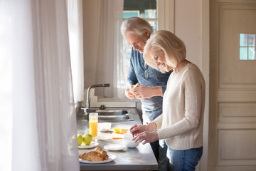 Happy senior husband and wife prepare healthy breakfast on kitchen, smiling aged couple make...