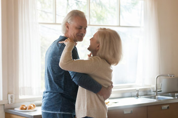 Smiling aged couple in love dancing in kitchen distracted from food preparing, happy senior husband...