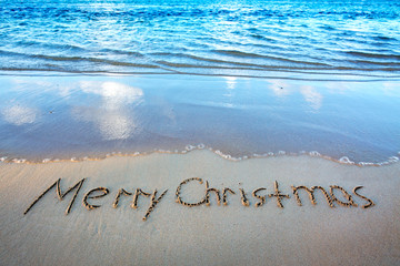 Word Merry Christmas written on the sand near the sea.
