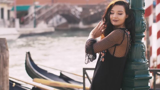 Seductive romantic woman standing on the pier against beautiful view on venetian chanal with boats and gondolas in Venice, Italy. Slow motion 4k footage. Gorgeous mixed race Asian Caucasian female in