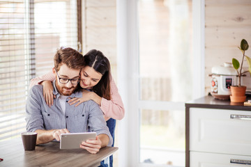 Happy young caucasian man in spectacles and woman in casual wear using tablet PC. Mid-aged excited couple using digital tablet choosing the kitchen furnishings.