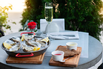 Fresh oysters with lemon's slices in ice and champagne. Restaurant delicacy, beautiful table setting. Saltwater oysters dish. Romantic dinner in restaurant.