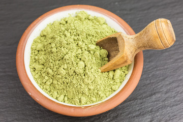 bowl of green matcha tea powder with wooden scoop
