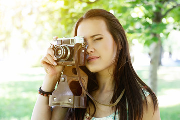 Cheerful beautiful girl talks pictures with vintage camera in summer park