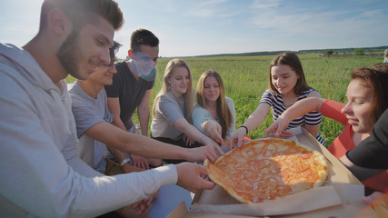 Friends of schoolchildren assort pizza outdoors during the sunset in the evening.