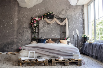 A wood bed in a photo studio decorated with flowers and curtains and sorrounded by books, frames, candle sticks