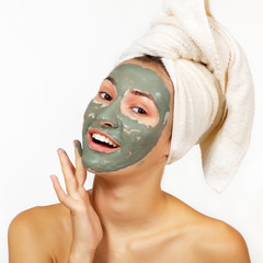 Beautiful cheerful teen girl applying facial clay mask. Beauty treatments, isolated over white...