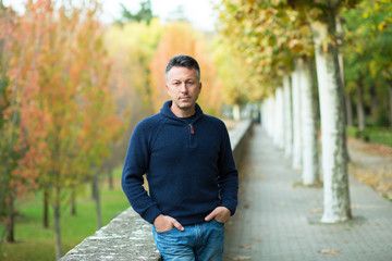 Handsome middle-aged man walking autumn park. Urban male portrait, image toned and noise added.