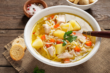 Chicken soup with noodles and vegetables in white bowl on  wooden background