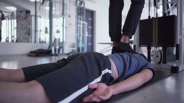 Legs of the male are treading on the back of laying man in the gym People in the gym Fitness Therapy