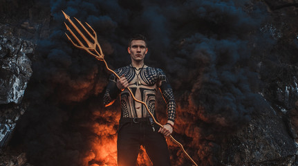 A young man with a trident against the background of fire and smoke.
