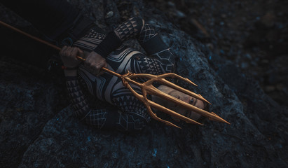 A young man with a trident in his hands lies on the rock.